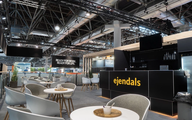 Messestand mit Sitzgruppen und Tresen mit beleuchtetem Schriftzug 'ejendals' auf einer Messe für Arbeitssicherheit.
