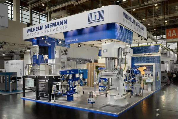 [Translate to English:] Messestand von Wilhelm Niemann mit großflächiger Maschinenpräsentation und markantem Deckenelement auf der Messe.