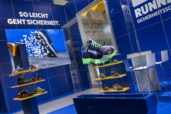  Großes Schuhmodell in Glasvitrine mit Sitzbereich im Hintergrund.