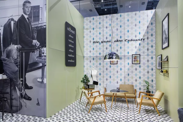 Stilvoll eingerichtete Lounge mit Retro-Sesseln und geometrischer Tapete im Messestand von Act’o-soft