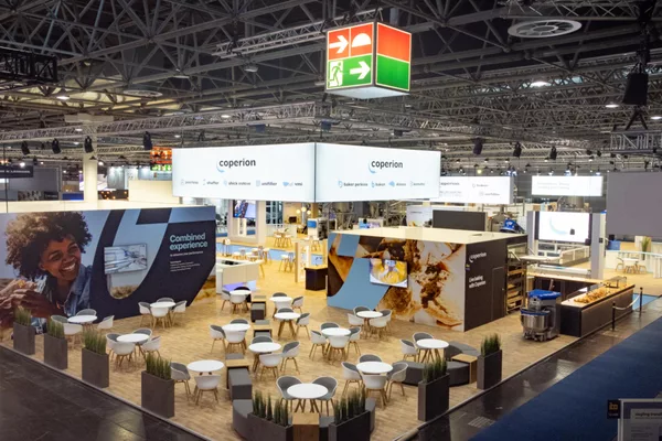 Top view of exhibition stand with many round tables, large ceiling banners “coperion” and baking area with oven station