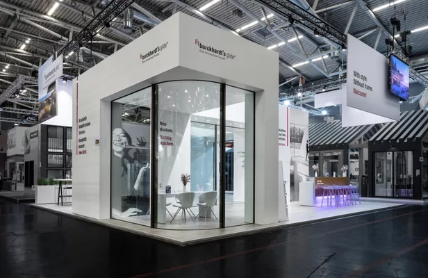 Ecke des Messestands mit großem Glasfenster und Sitzbereich innen.