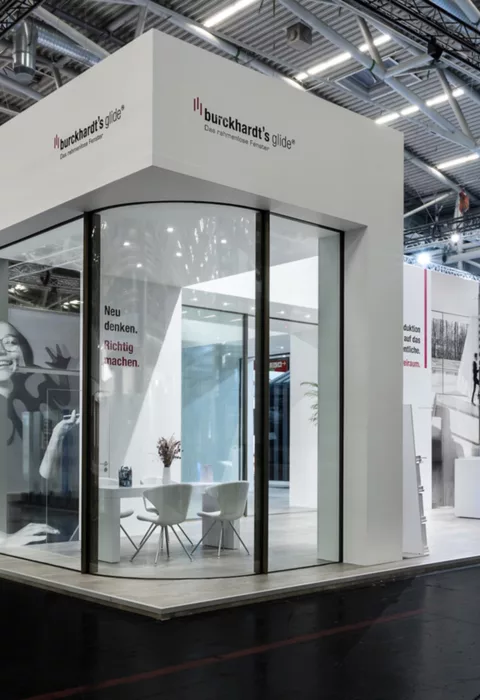 Ecke des Messestands mit großem Glasfenster und Sitzbereich innen.