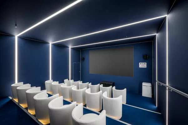 Kinoraum mit weißen Sesseln, LED-Lichtstreifen an Wänden und Decke sowie Projektionsfläche.