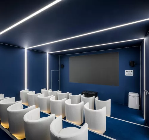 Kinoraum mit weißen Sesseln, LED-Lichtstreifen an Wänden und Decke sowie Projektionsfläche.
